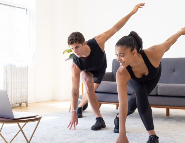 Man and Woman touch the floor while exercising in front of their trainer on a laptop